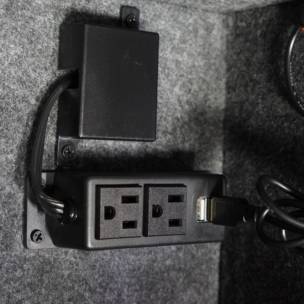 Dual electric outlet with USB port installed in a gray felt interior, ideal for powering devices.