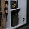 Image of Fireproof gun safe displayed on a shelf, featuring a green ammo can and books on weapon care.